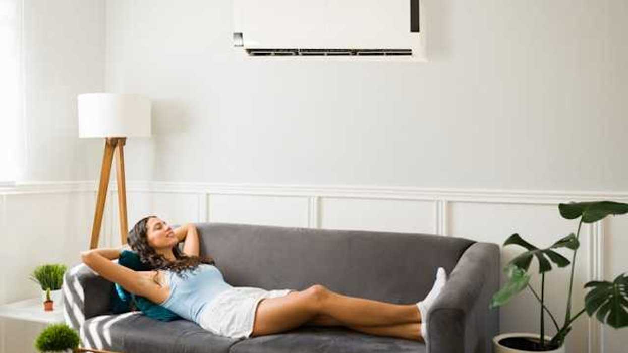 A woman lying on a couch under a wall mounted air conditioning unit