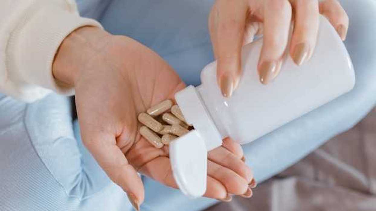 A woman opening a supplement bottle with pills pouring into her hand