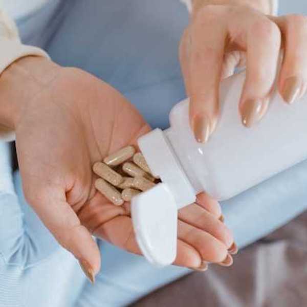 A woman opening a supplement bottle with pills pouring into her hand