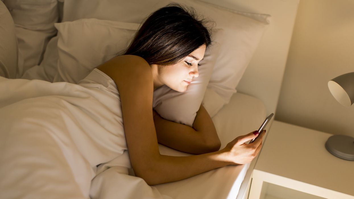 A woman reads her phone in bed
