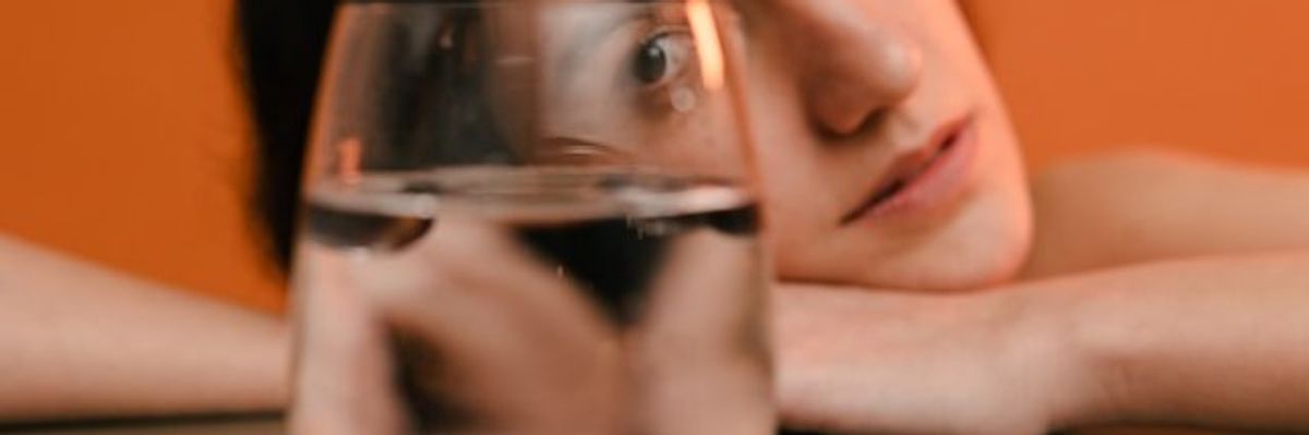 A woman resting her head on her hands looking at a glass of water.