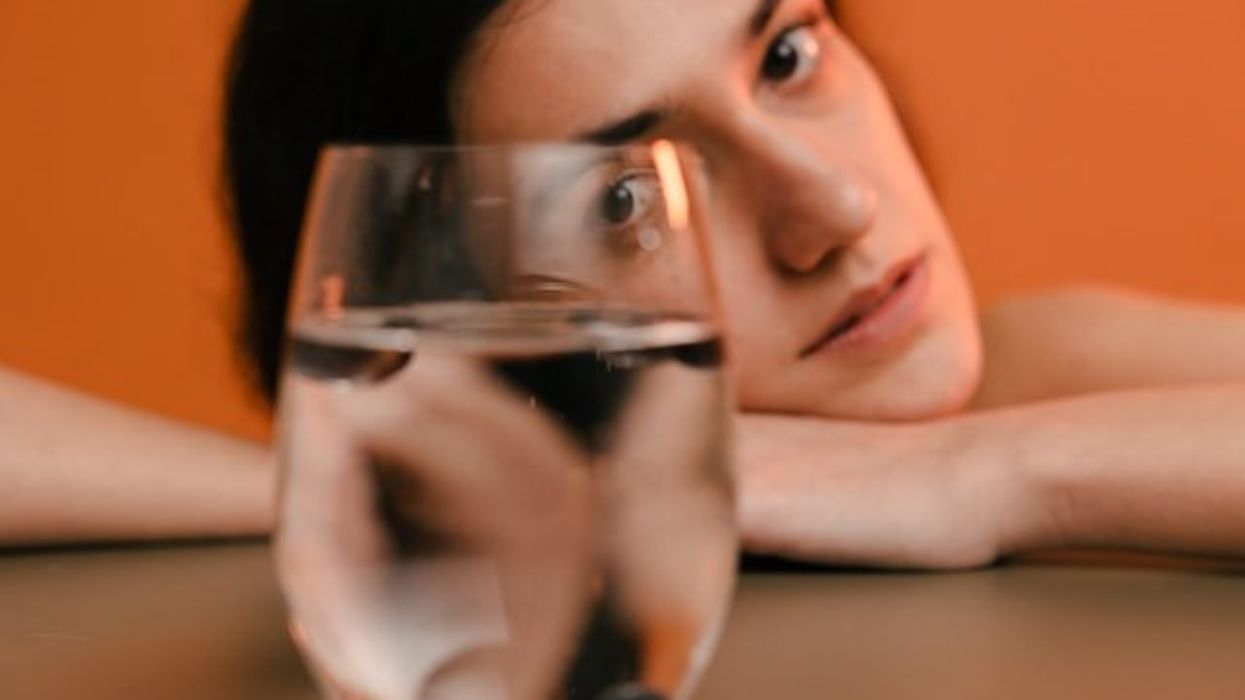 A woman resting her head on her hands looking at a glass of water.