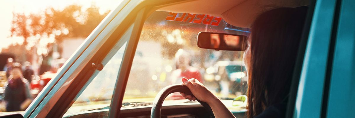 A woman sits in her car in the sun