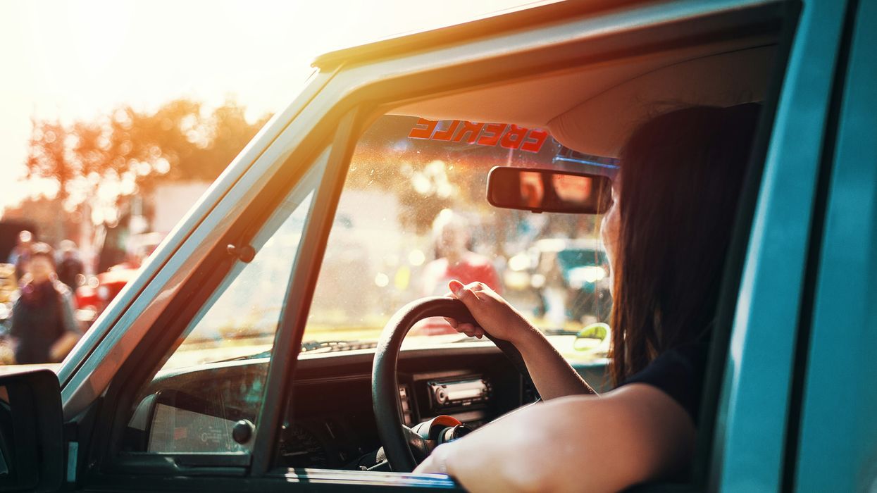 A woman sits in her car in the sun