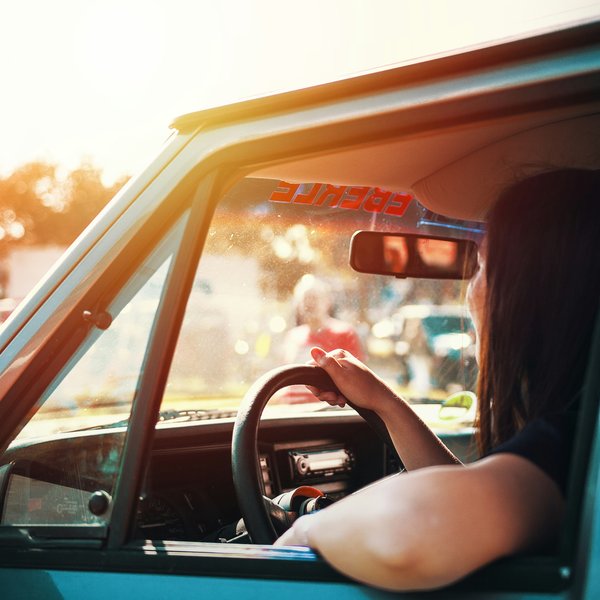 A woman sits in her car in the sun