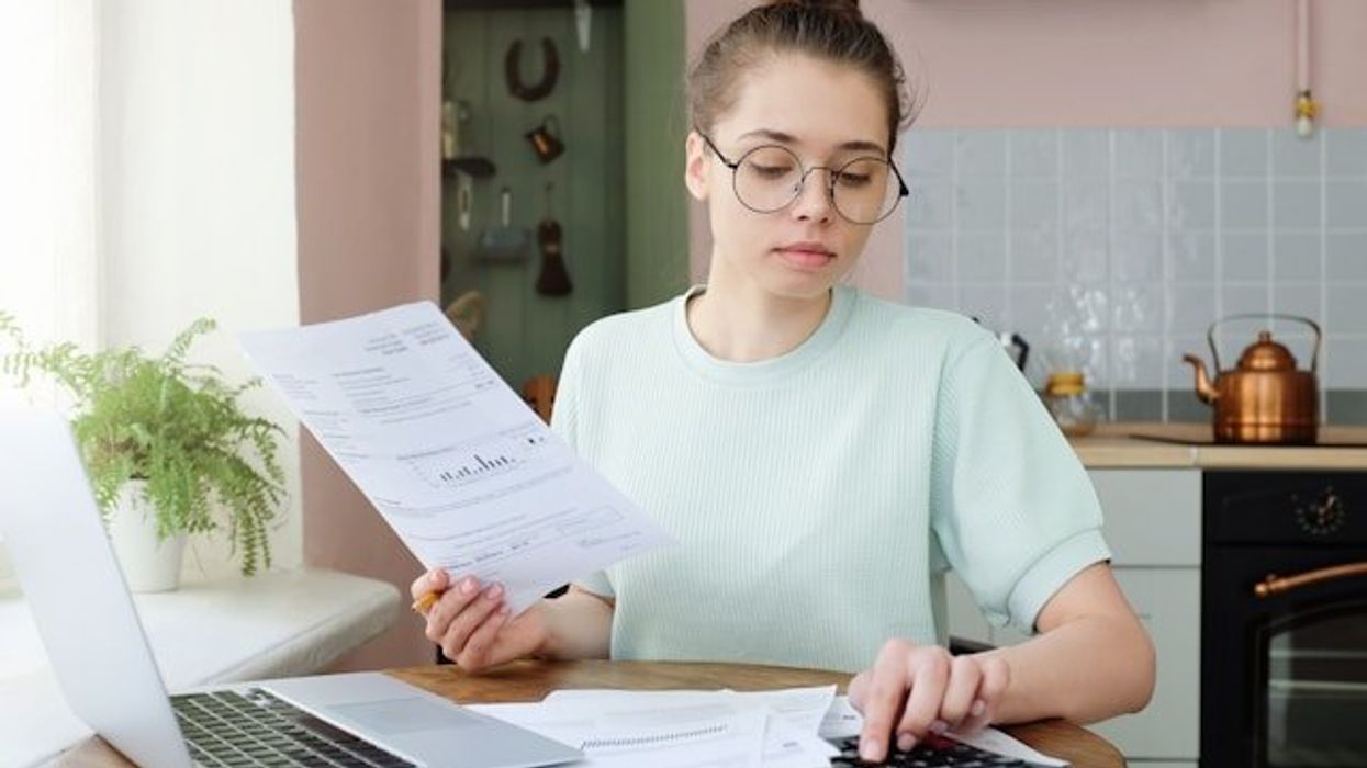 A woman sitting at a kitchen table with a utility bill and a calculator.