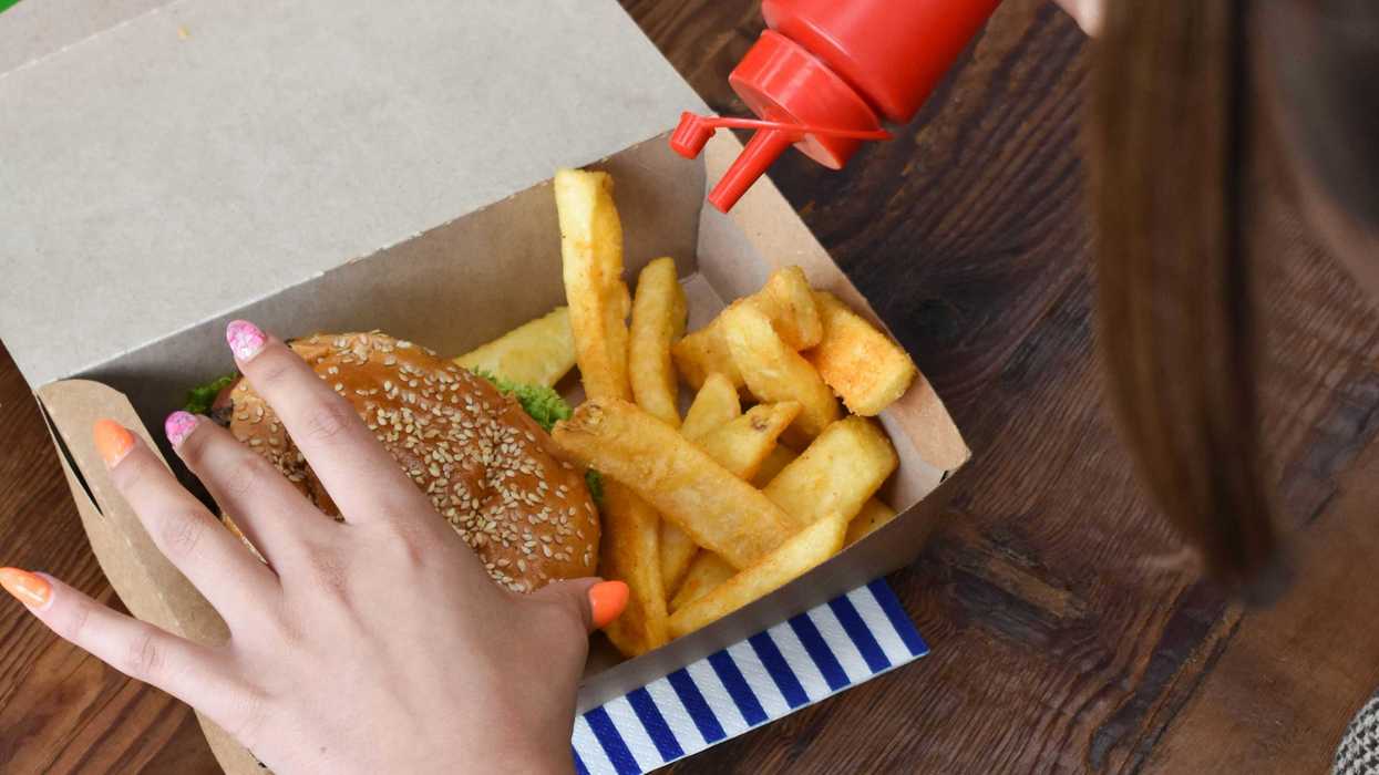 a woman sitting at a table with a box of fast food and a ketchup bottle.