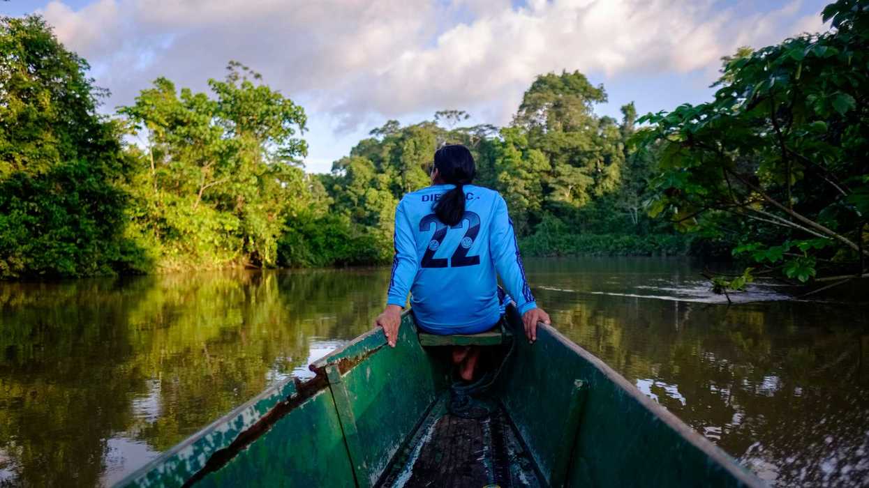 a woman sitting in a boat on a river flanked by trees.