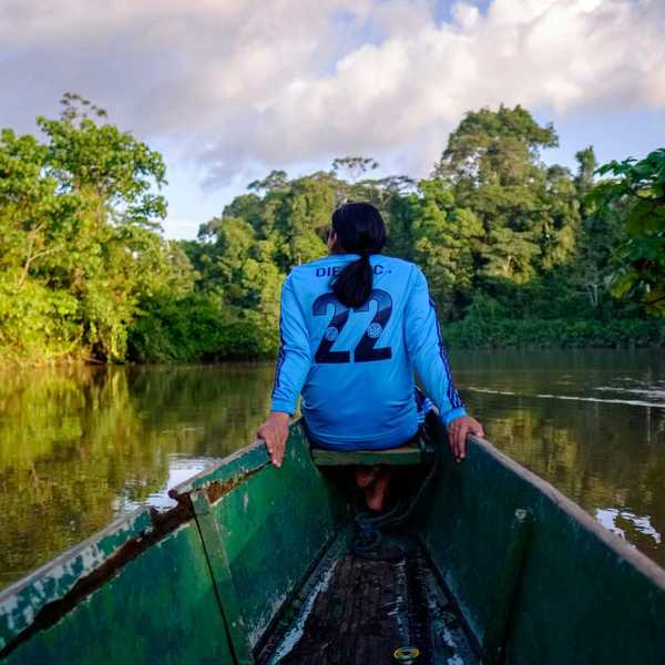 a woman sitting in a boat on a river flanked by trees.