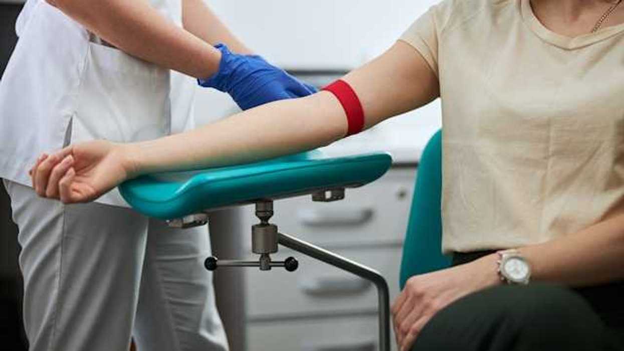 A woman sitting in a chair having her blood collected by a nurse