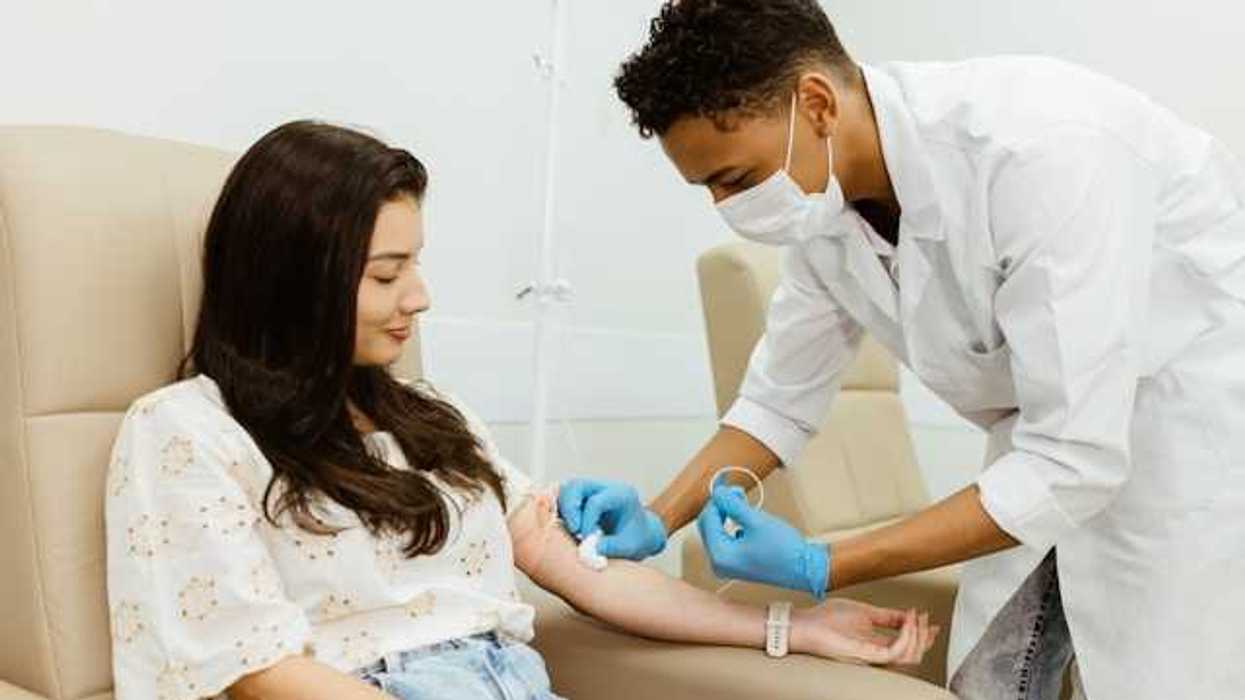 A woman sitting in a chair while a health worker preps her arm to draw blood