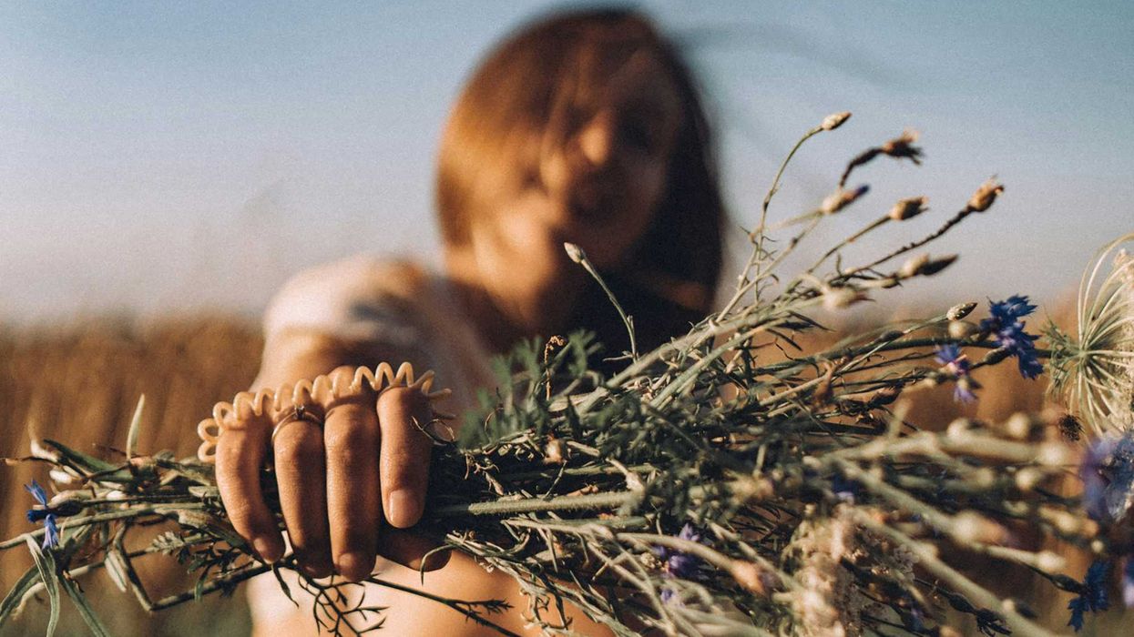 a woman sitting in a field holding a bunch of flowers.