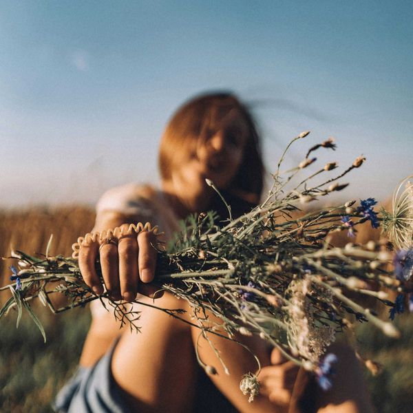 a woman sitting in a field holding a bunch of flowers.