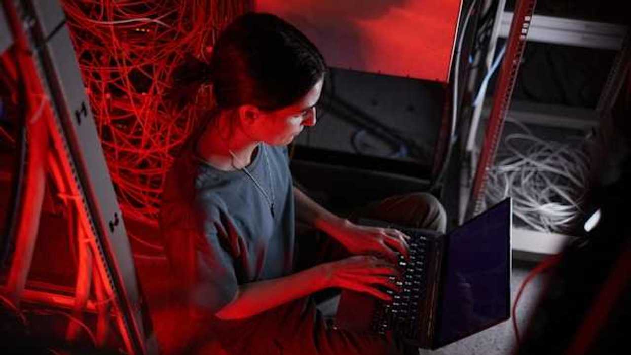 A woman sitting in front of a laptop with servers behind her