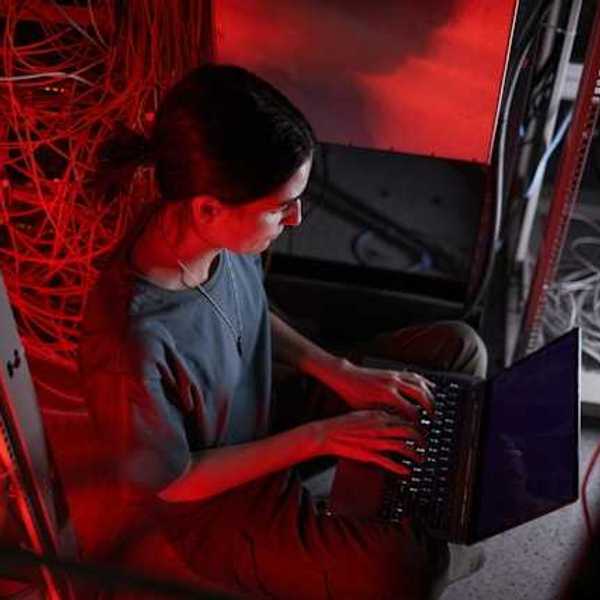 A woman sitting in front of a laptop with servers behind her