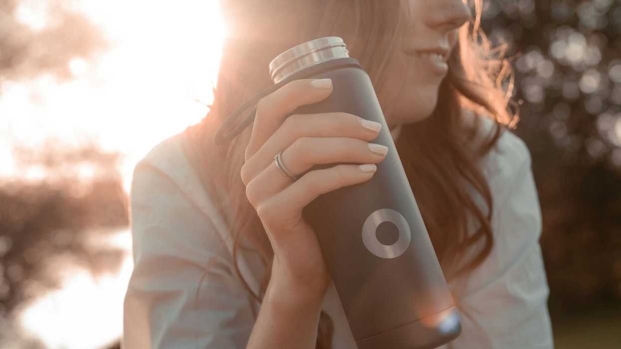 a woman sitting on a bench holding a stainless steel water bottle.