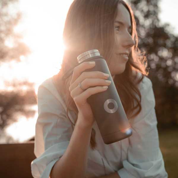 a woman sitting on a bench holding a stainless steel water bottle.
