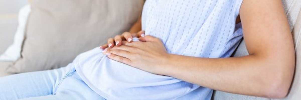 A woman sitting on a couch with her hands on her belly.