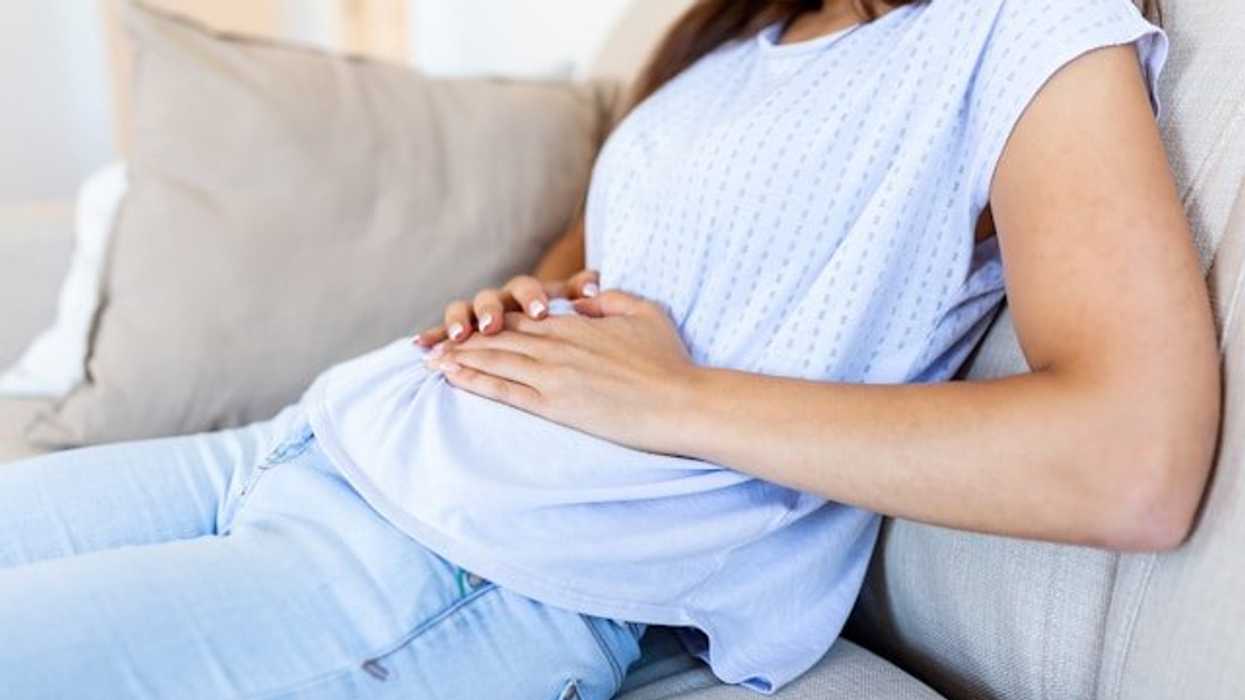 A woman sitting on a couch with her hands on her belly.