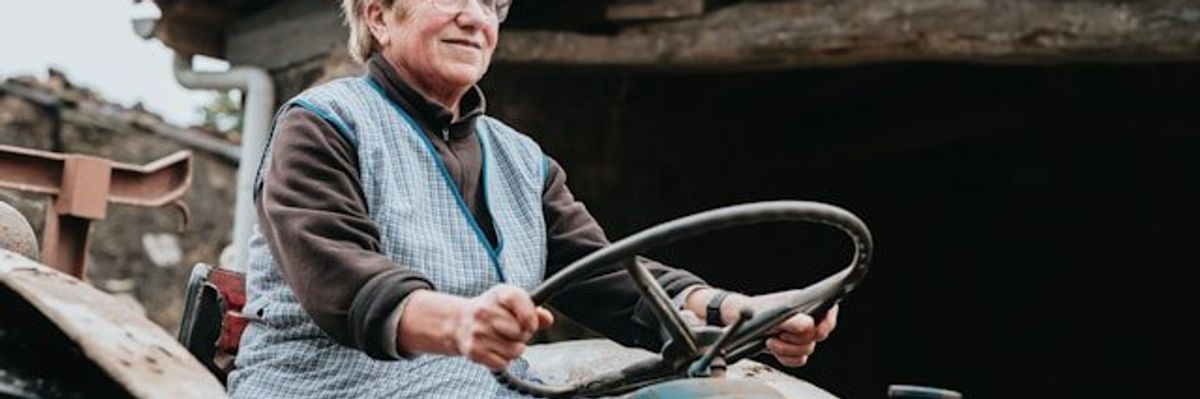 A woman sitting on a tractor in front of a wooden barn.