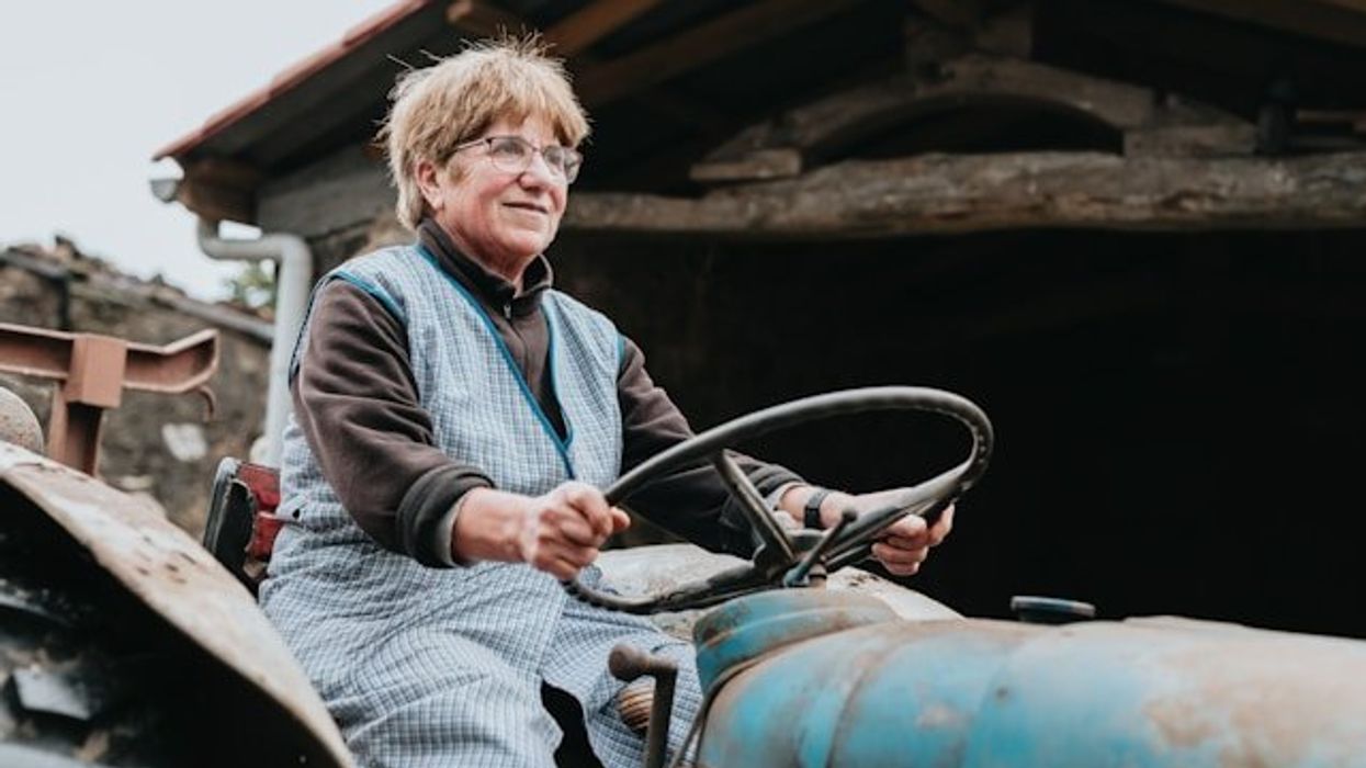 A woman sitting on a tractor in front of a wooden barn.