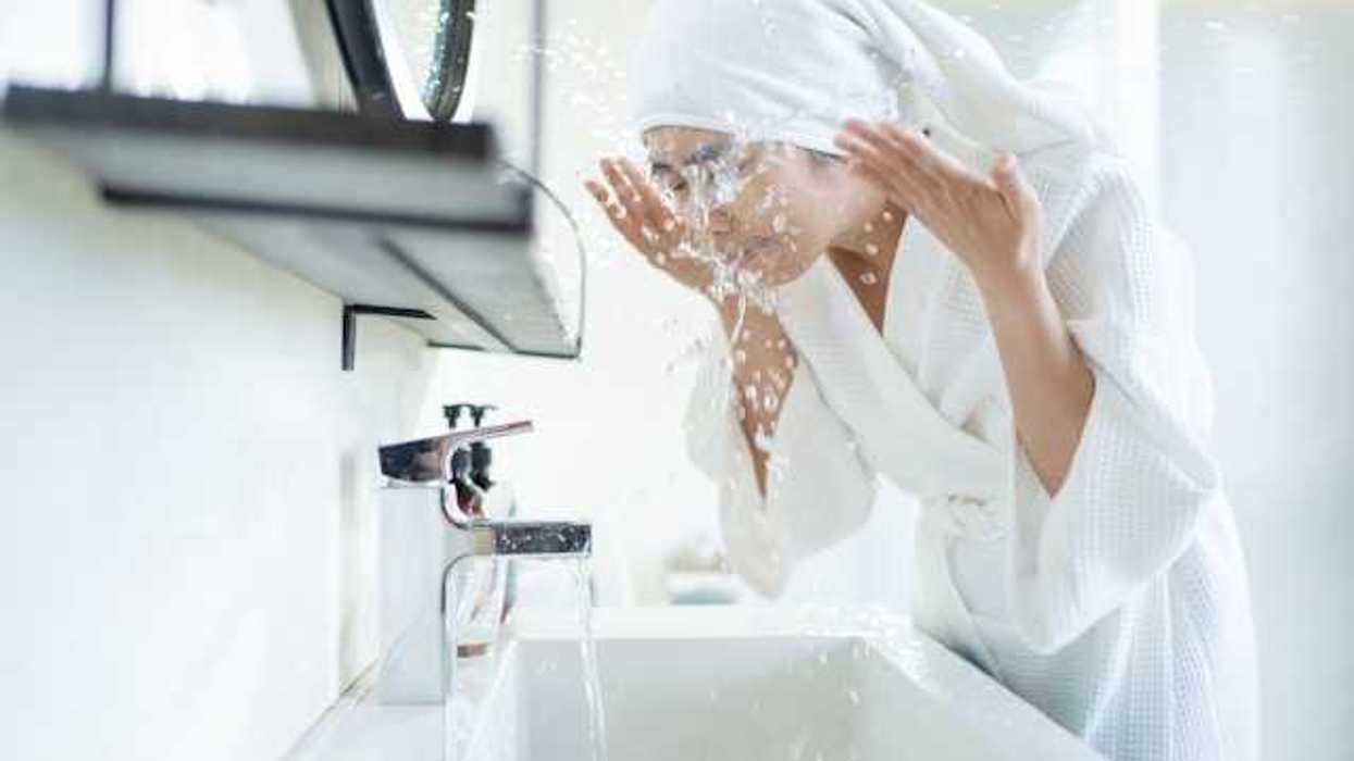 A woman splashing water onto her face in a bathroom