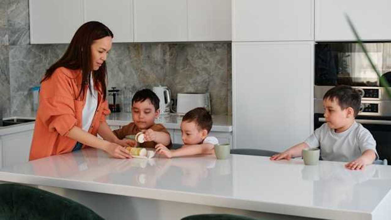 A woman standing at a kitchen counter with three small children looking at cookies