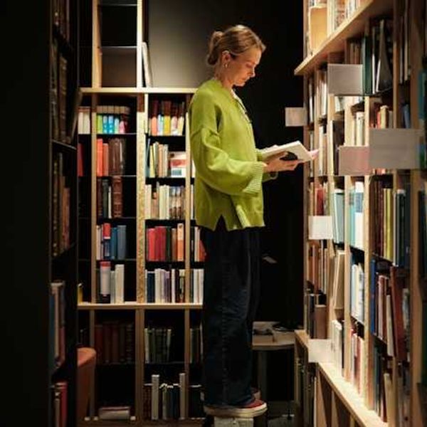 A woman standing on a stool in front of library bookshelves