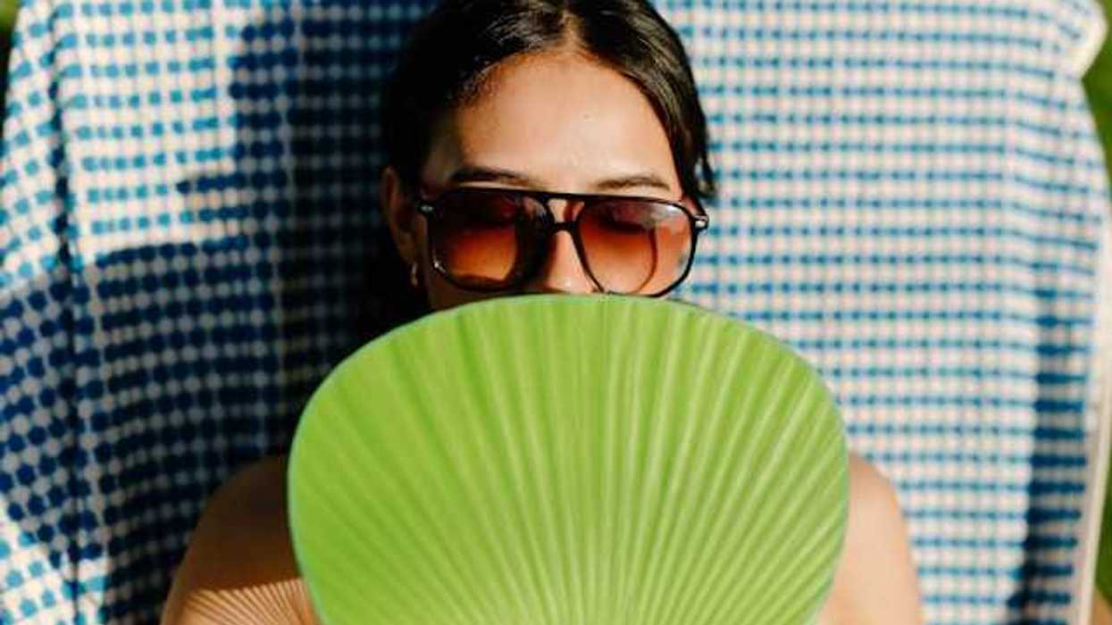 A woman sunbathing with a green handheld fan shading her chest and lower face