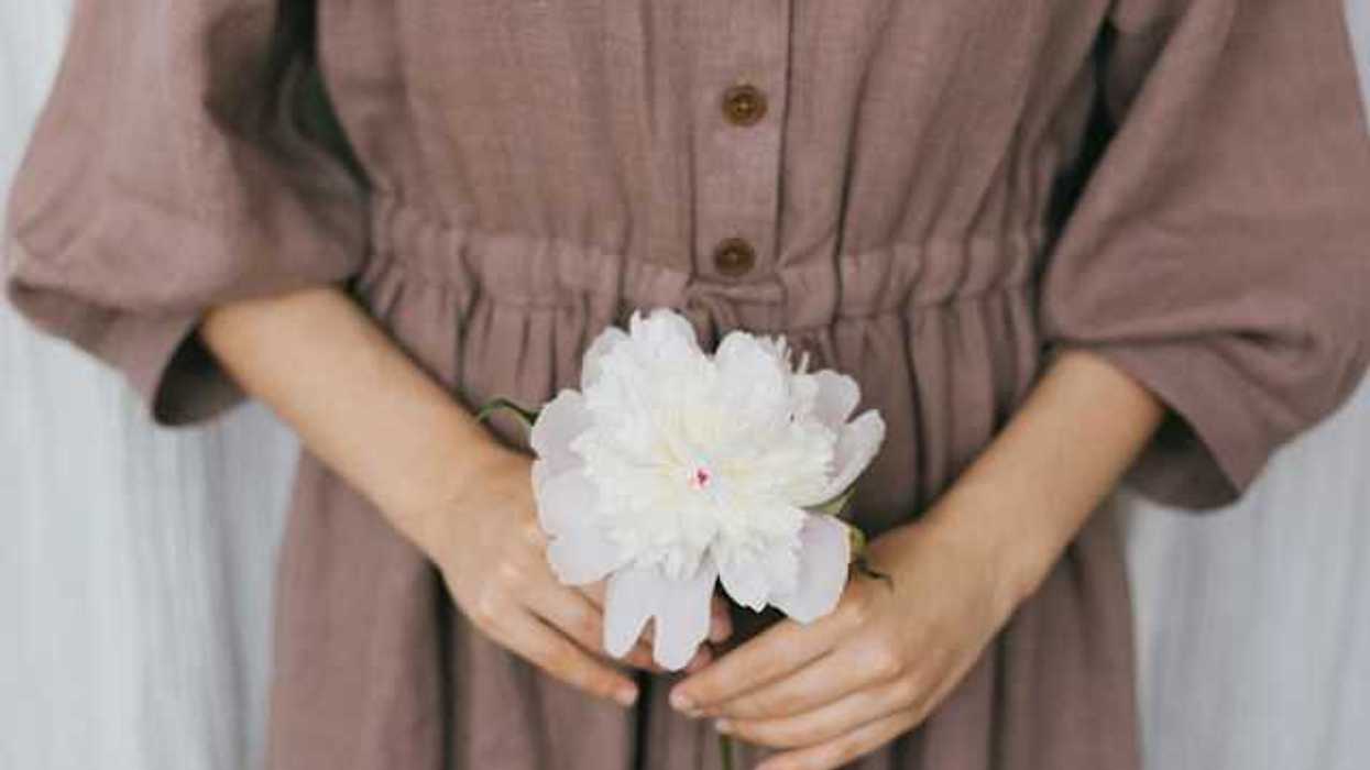 A woman wearing a brown linen dress holding a white flower