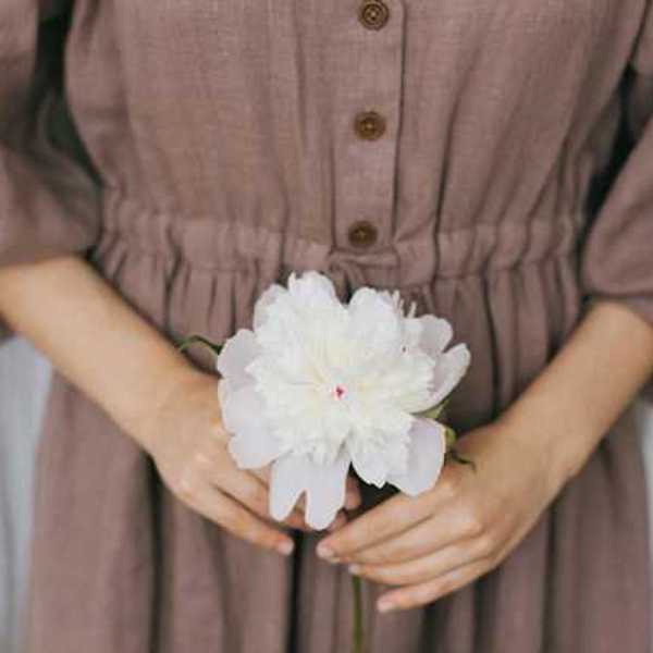 A woman wearing a brown linen dress holding a white flower