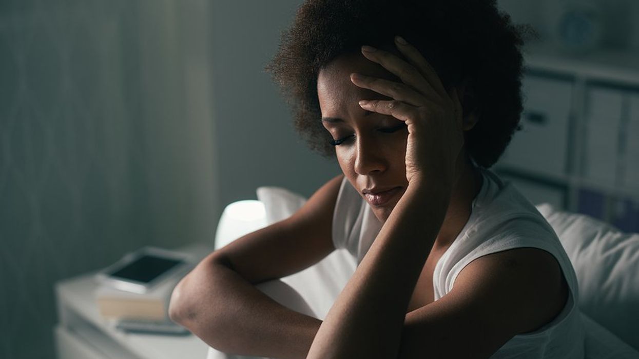 A woman wearing a tank top sitting up in bed with her hand to her forehead.