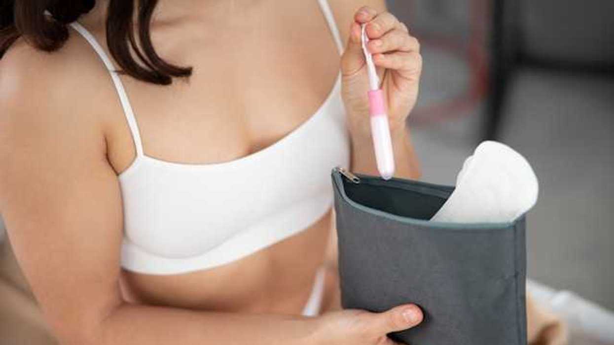 A woman wearing a white sports bra putting a tampon and a menstrual pad in her purse