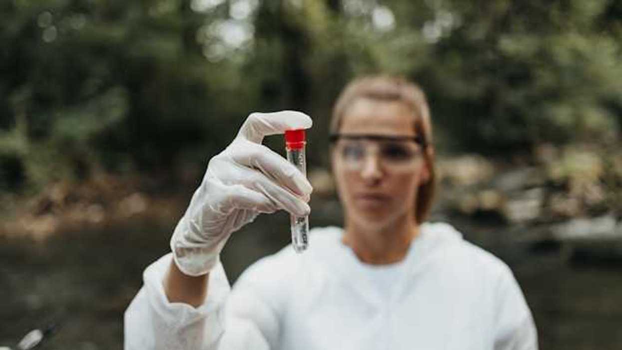 A woman wearing white overalls and safety glasses holding a beaker of water