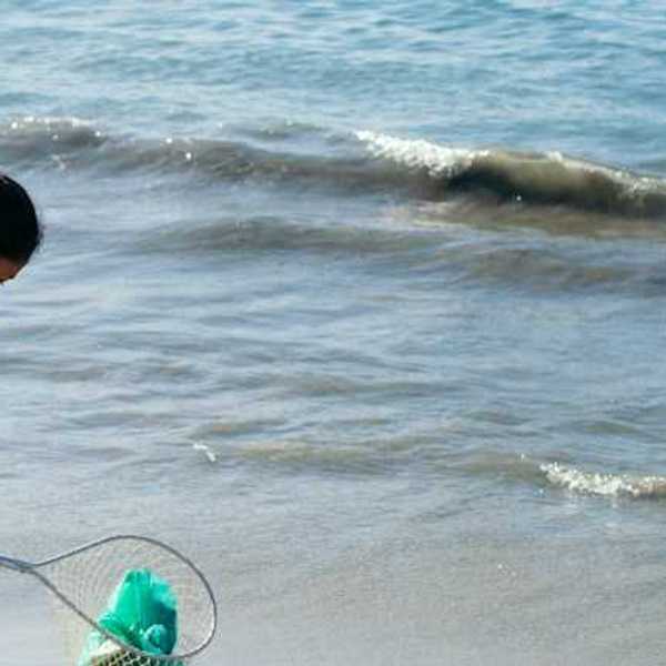 A woman with a net cleaning up plastic bags from the beach