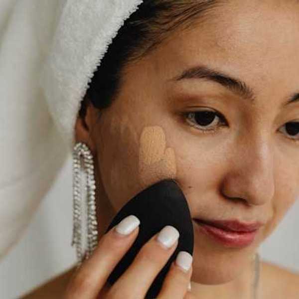 A woman with a white towel on her head applying foundation to her face