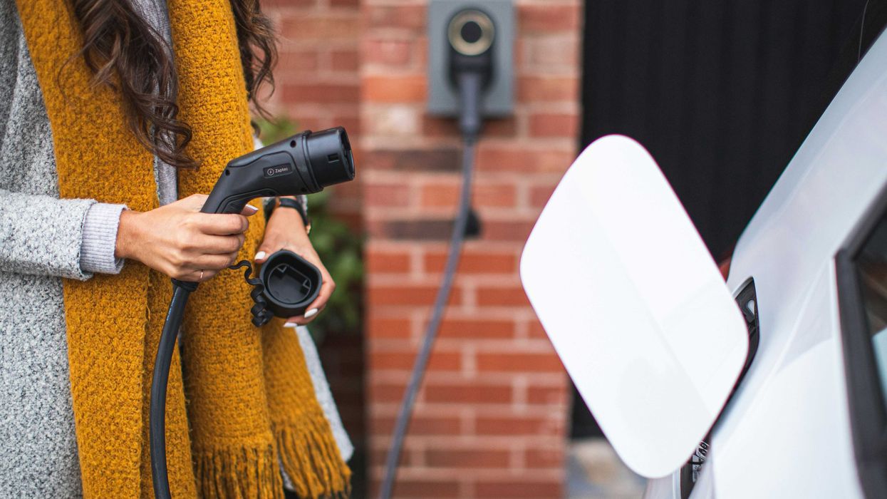 a woman with a yellow scarf attaching an electric vehicle charger to her car