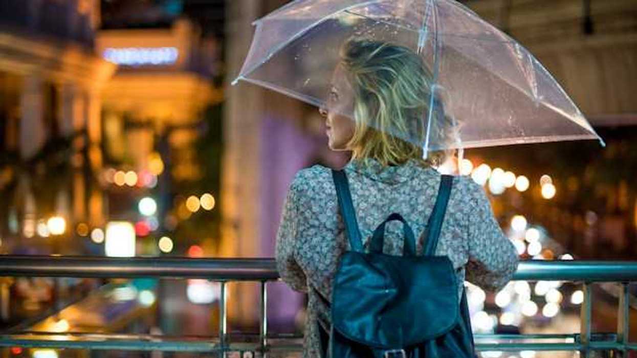 A woman with an umbrella looking out over a city street at night