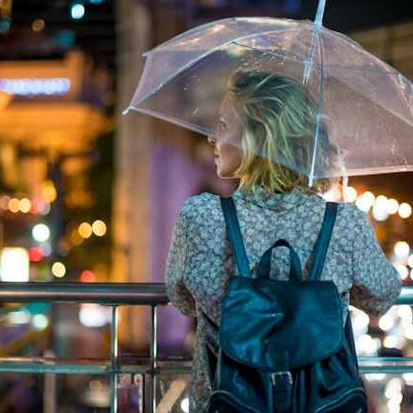 A woman with an umbrella looking out over a city street at night