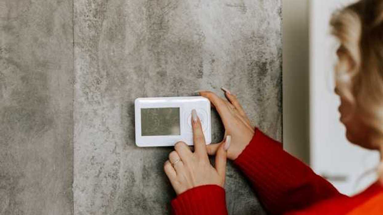 A woman with her finger on a wall thermostat, changing the temperature