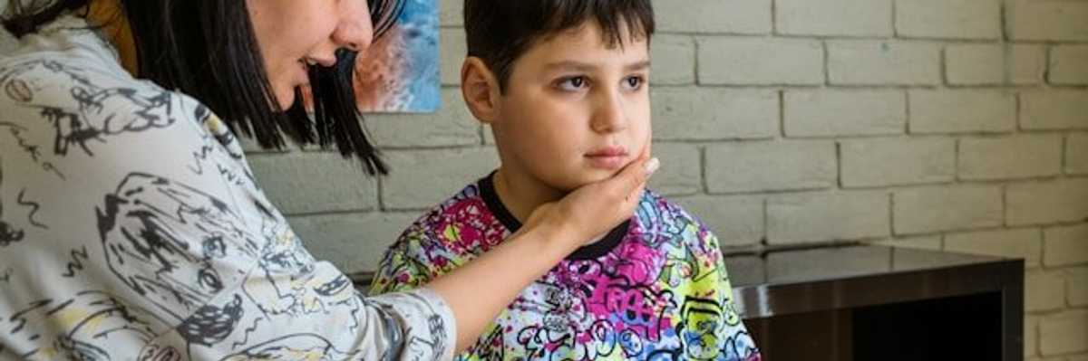 A woman with her hand on the face of a child who is looking straight ahead.