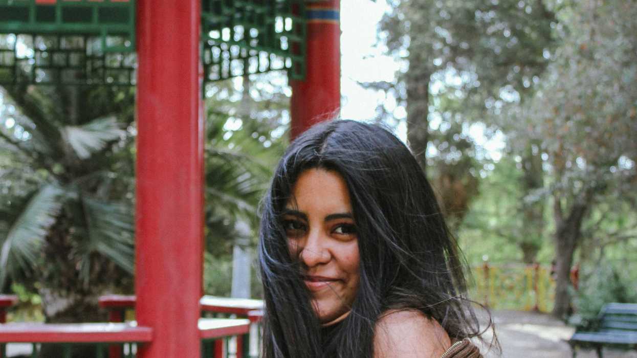 a woman with long dark hair smiles with trees and park benches in background.