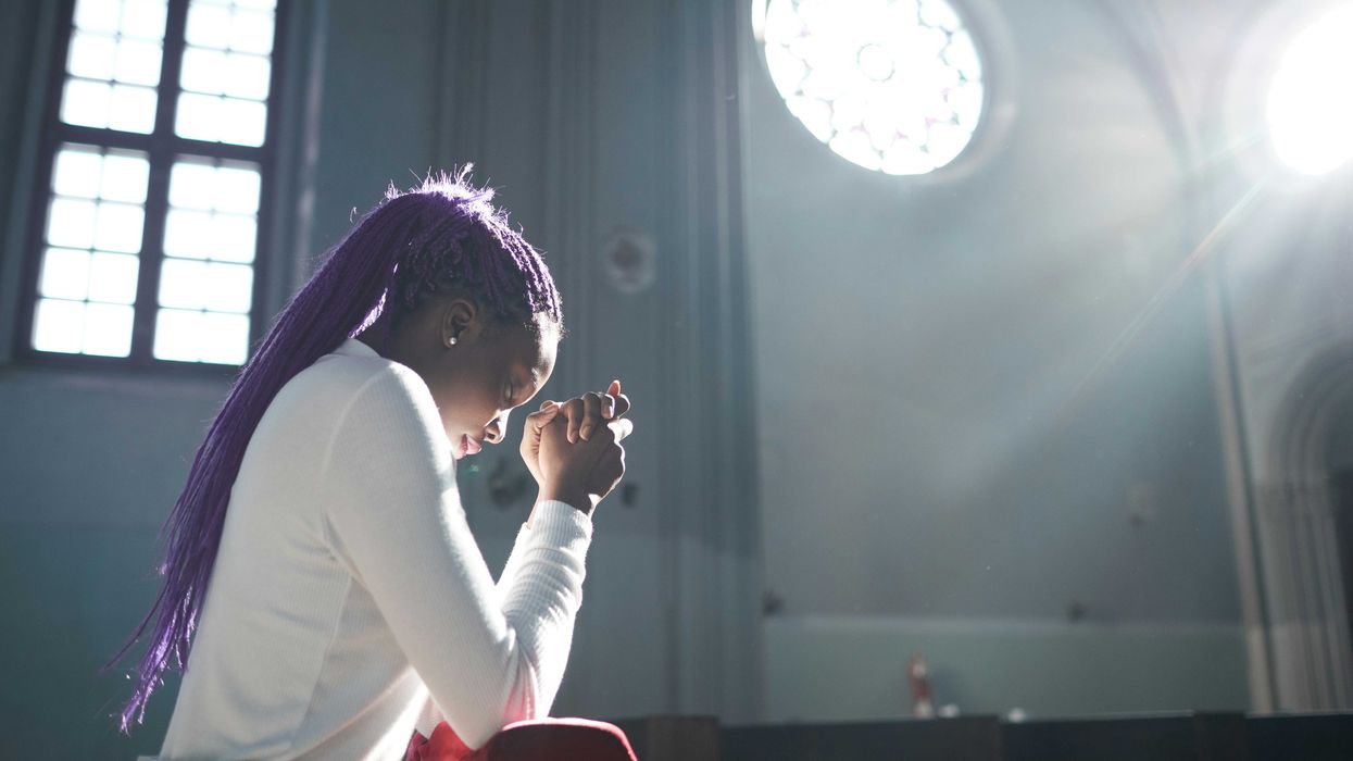 A woman with long purple dreadlocks prays inside a church.