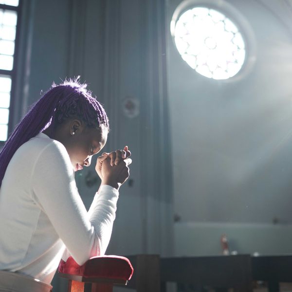 A woman with long purple dreadlocks prays inside a church.