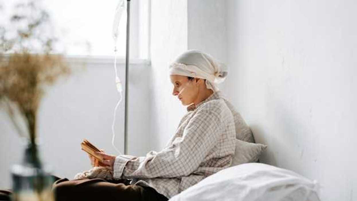 A women sitting on a bed reading a book with an IV hooked up