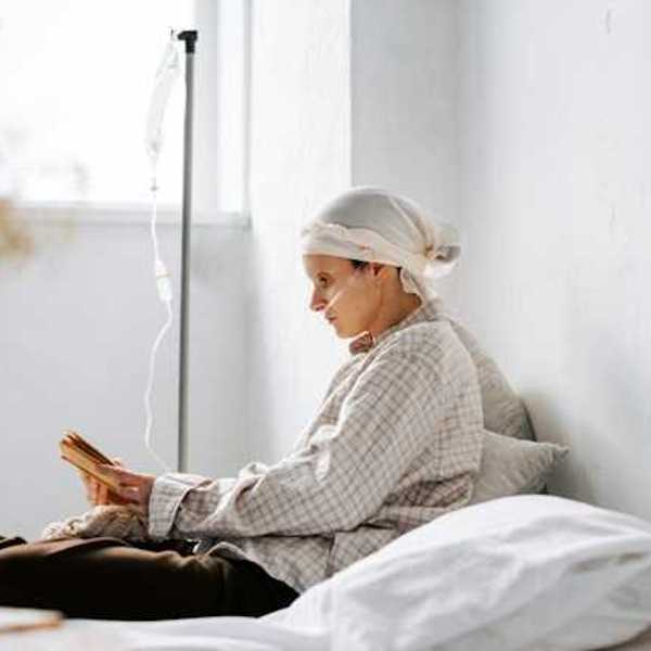 A women sitting on a bed reading a book with an IV hooked up