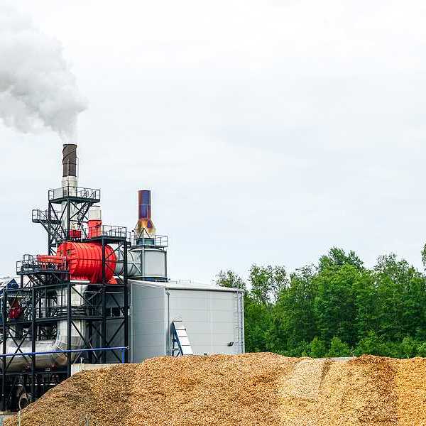 A wood pellet plant with a pile of wood pellets in front of an industrial machine