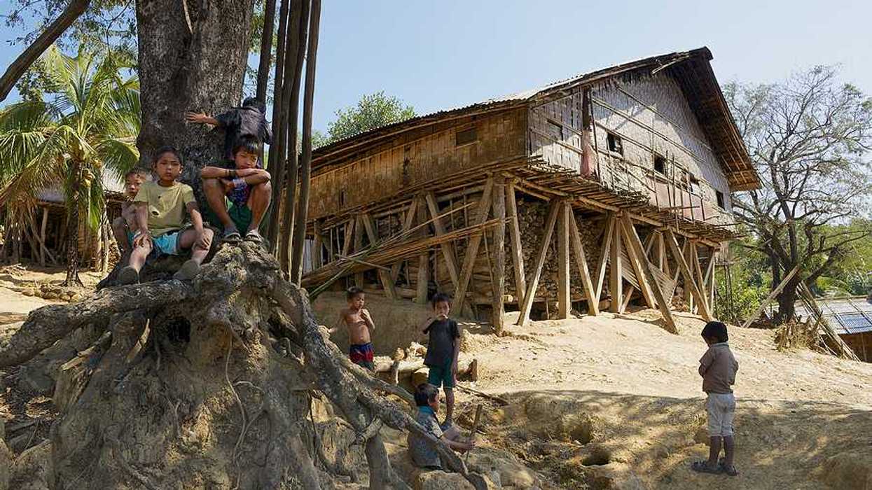 A wooden hut located on a hill with small children playing in the dirt in front of it