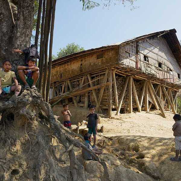 A wooden hut located on a hill with small children playing in the dirt in front of it
