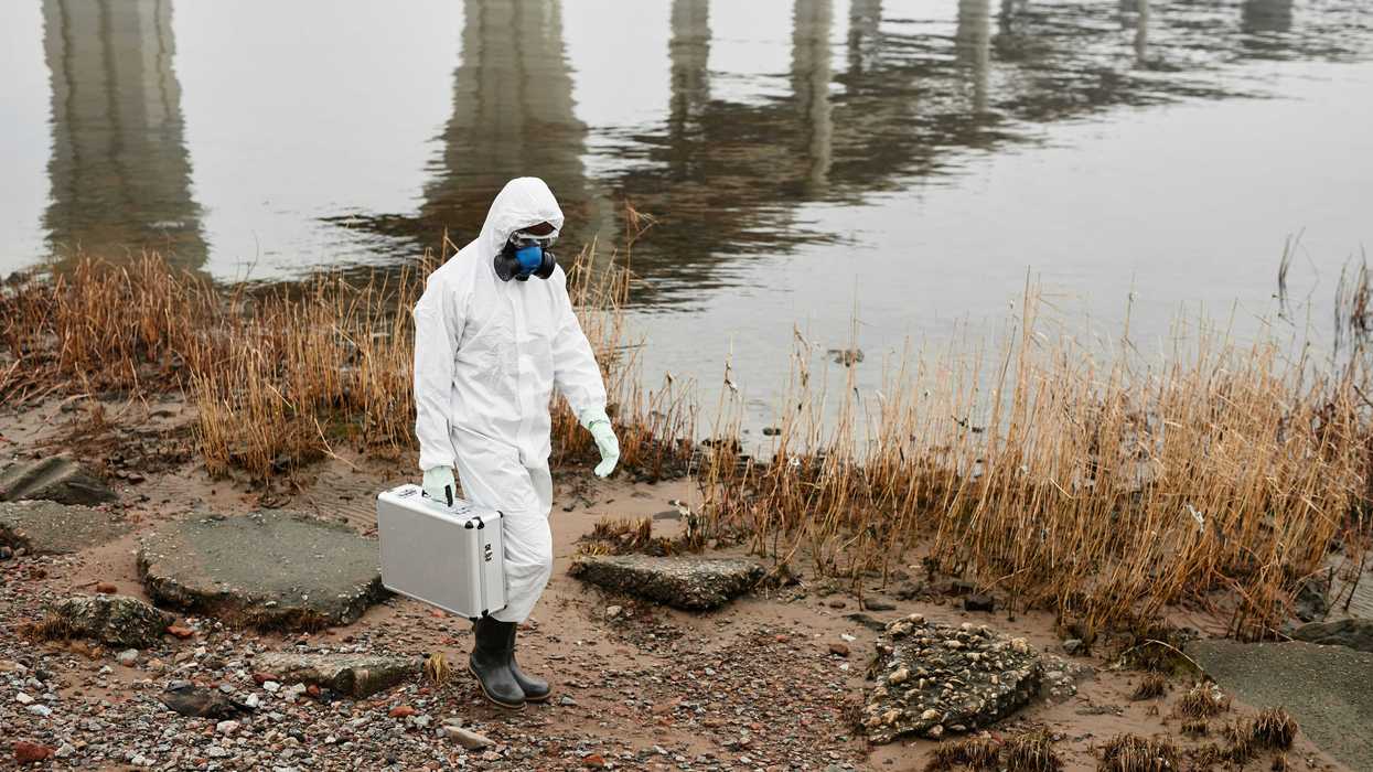 A worker in a Hazmat suit walking near a body of water